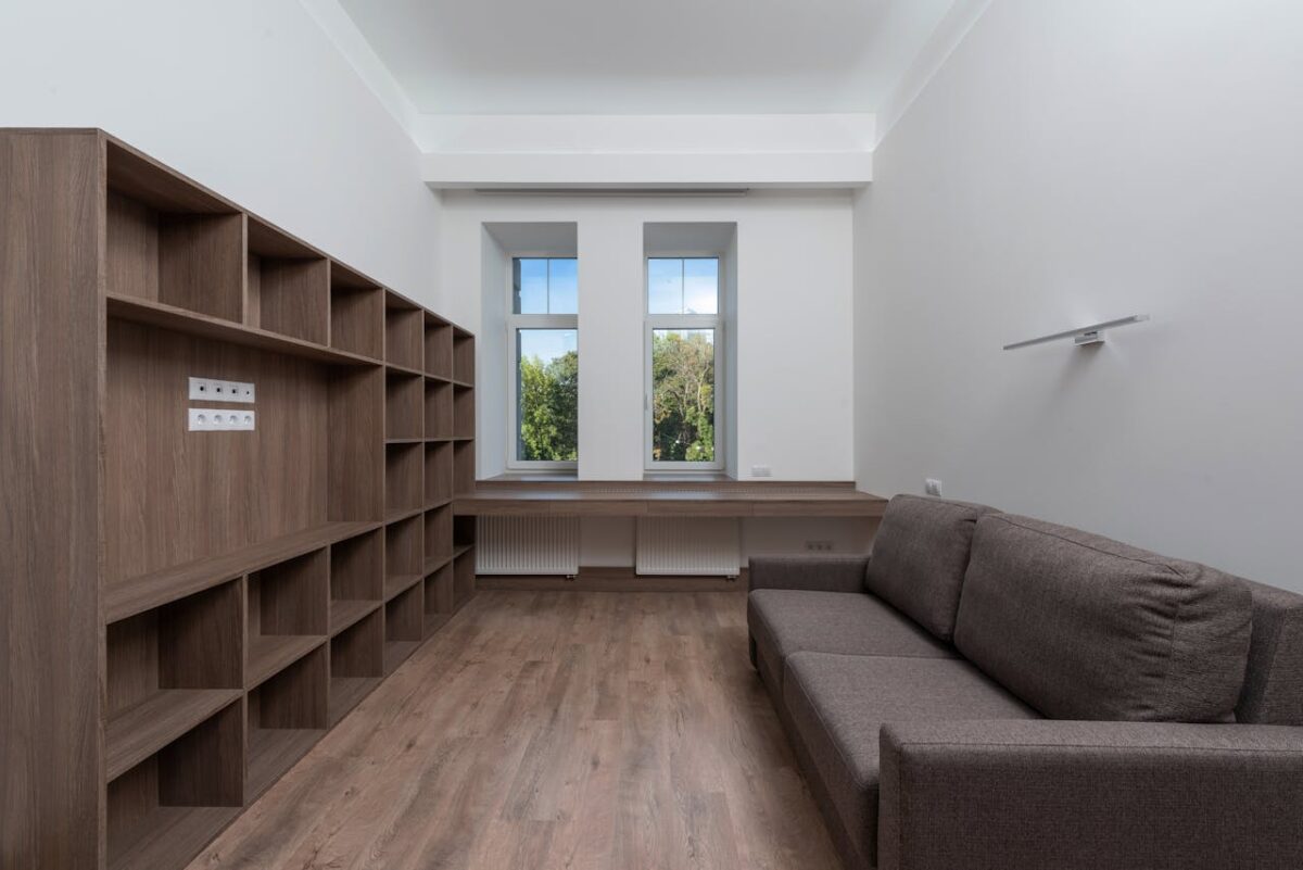 Modern minimalist living space with wooden shelves, sofa, and large windows for natural light.